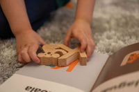 Child playing with wooden letter K, and koala, on an open book on a carpeted floor