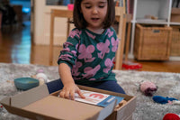 Child opening a cardboard box on a carpeted floor