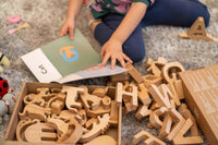 Child playing with wooden letters and a book on the floor.