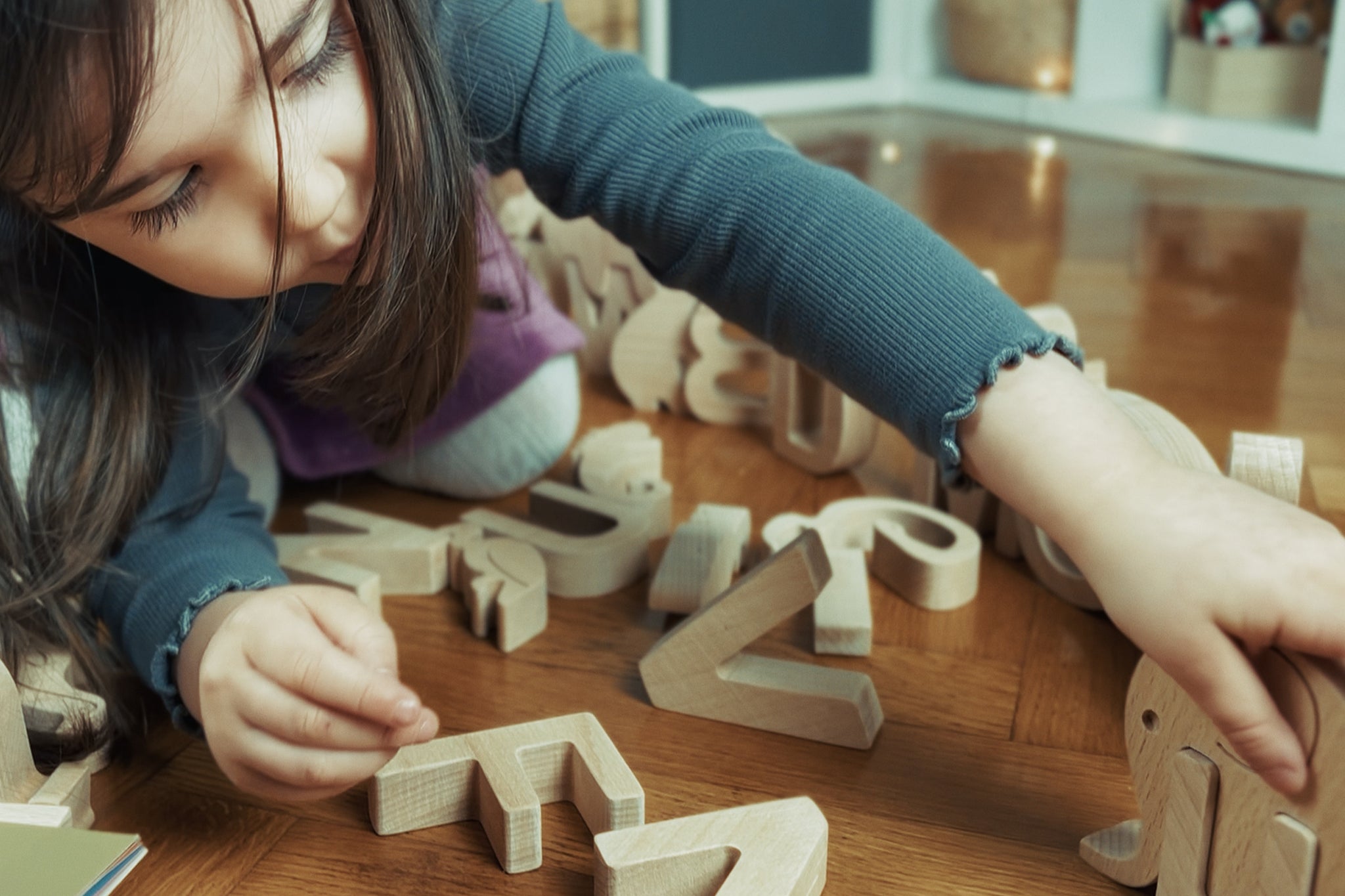 Child playing with wooden letters on a wooden floor