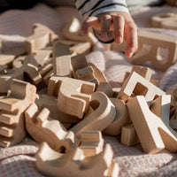 Child's hand reaching towards wooden letter blocks on a soft surface