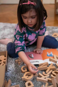 Child playing with wooden letters on a carpeted floor