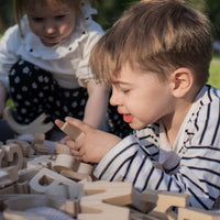 Two children playing with wooden letters outdoors.