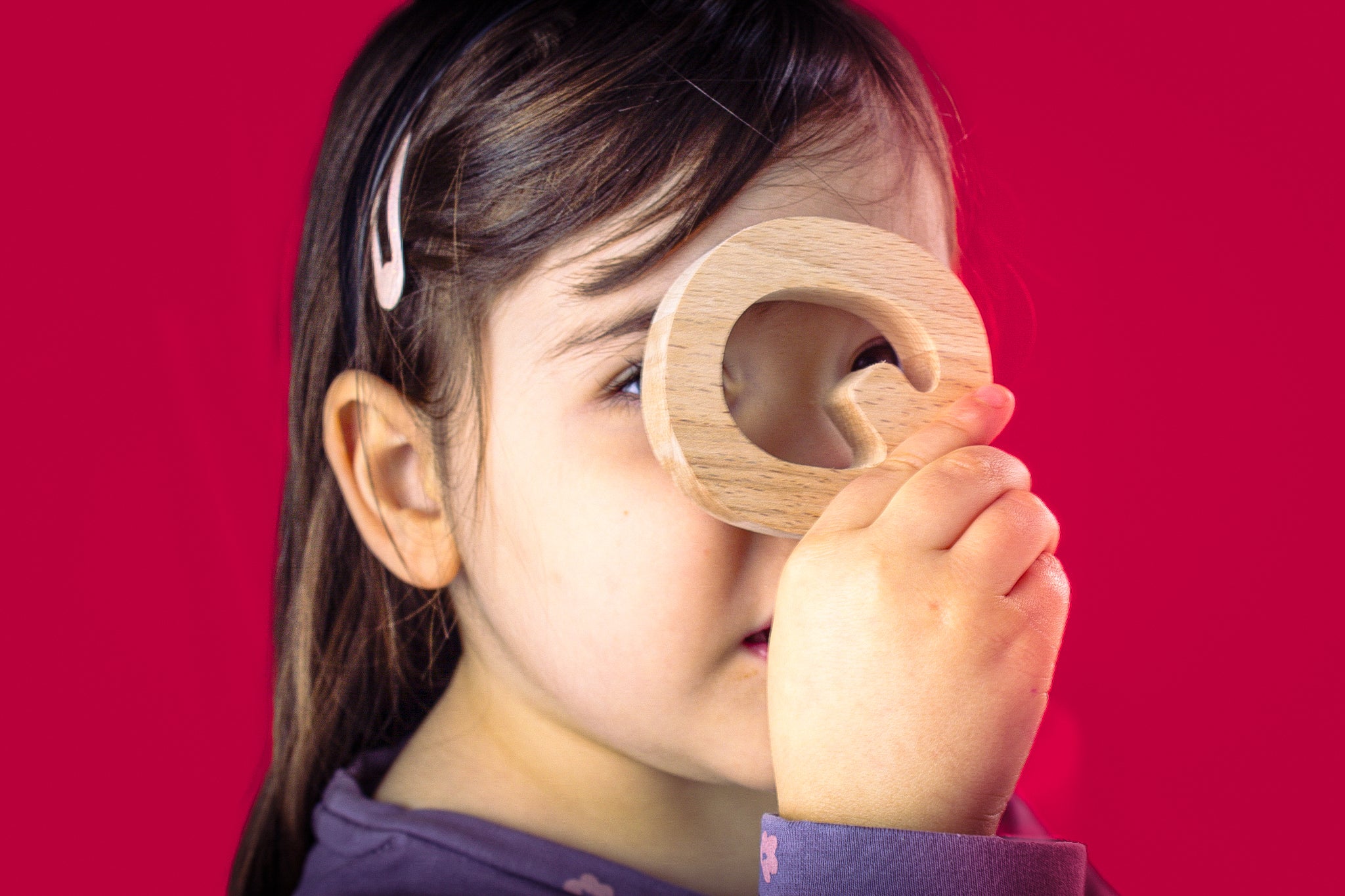 Child holding a wooden letter 'Q' against a red background